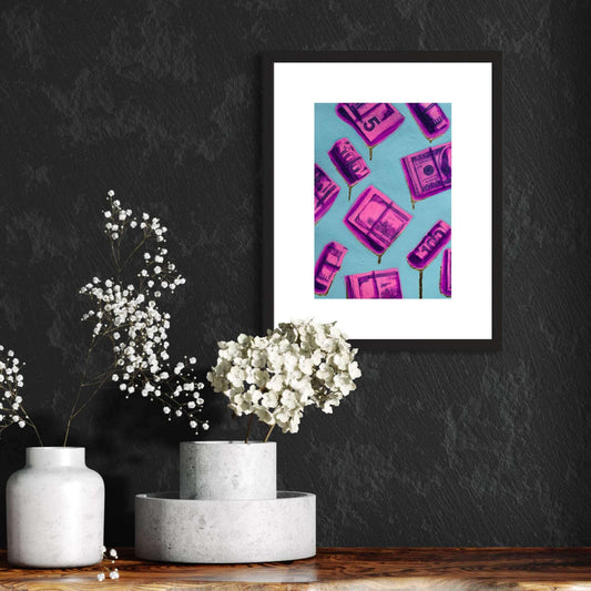 A framed painting featuring hot pink and purple dollar bills on a blue background, displayed on a wall above a grey marble table with a vase of flowers.
