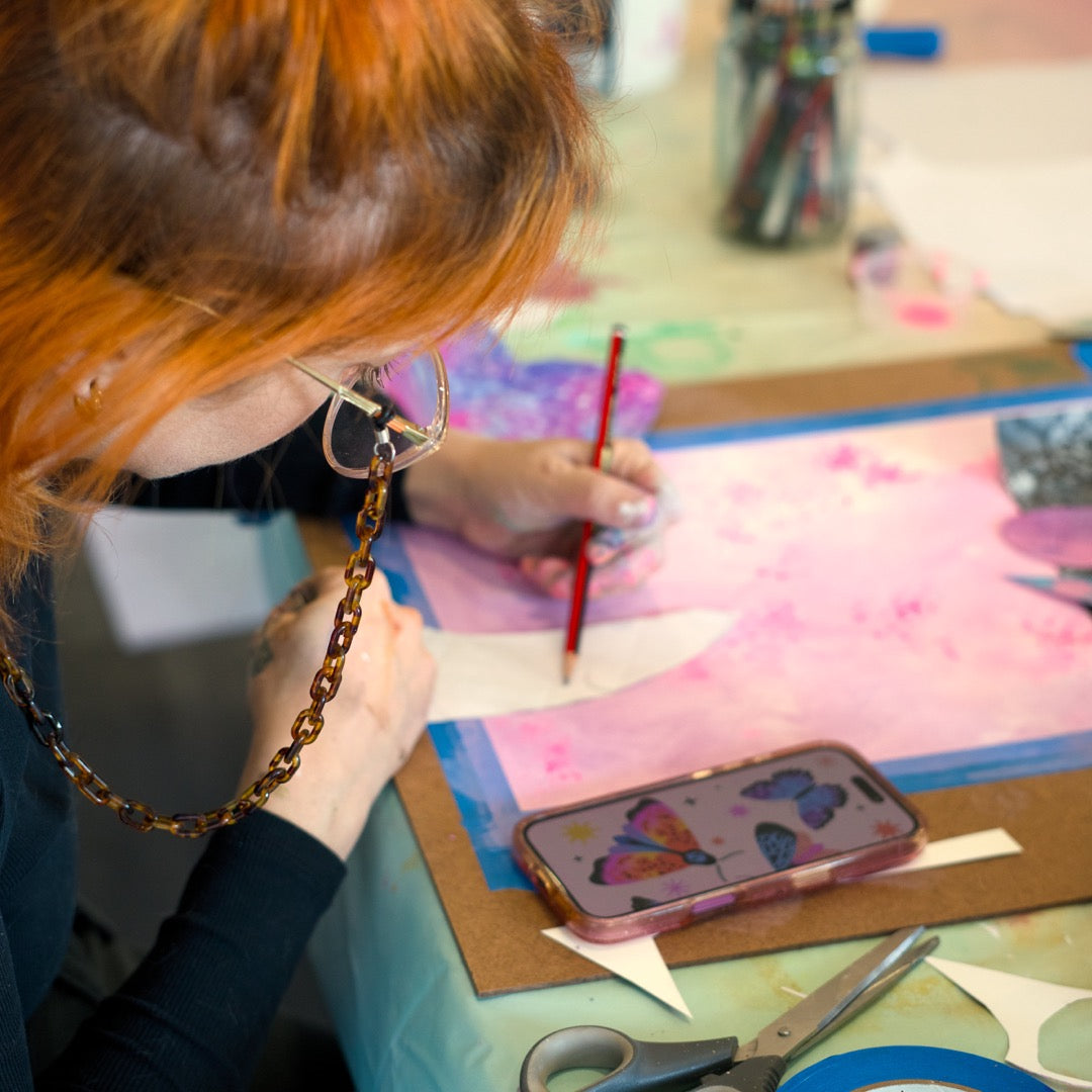 Person with red hair painting on a table with art supplies. Art classes in Berwick