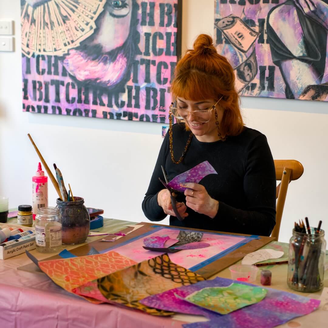 Art Classes Berwick, Narre Warren, Clyde North. Painting Classes Criss Chaney. Woman working on art at a table with colorful materials and artwork in the background.