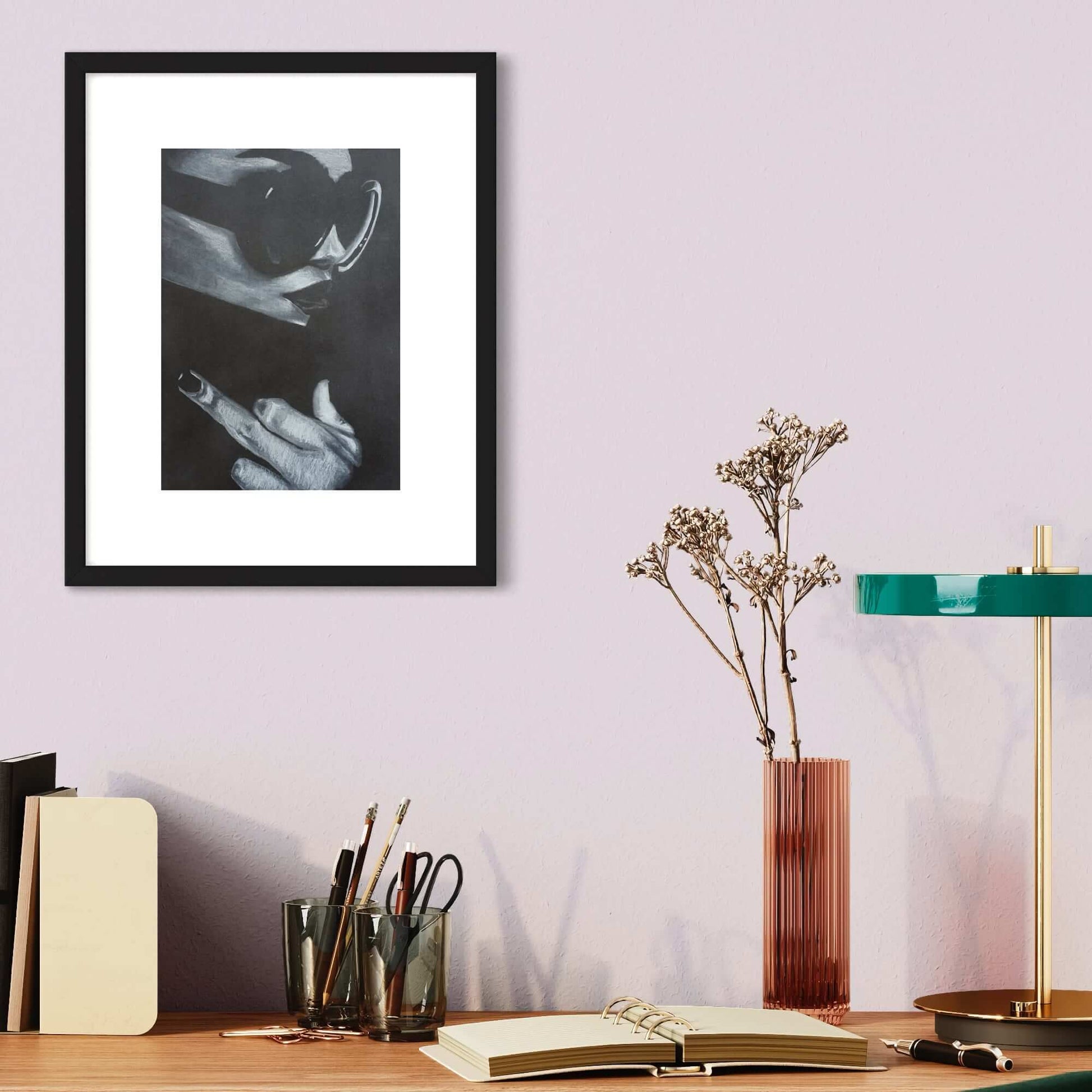 A framed artwork depicting a black and white image of a woman making a 'middle finger' gesture, placed on a table with books and a lamp in the background.