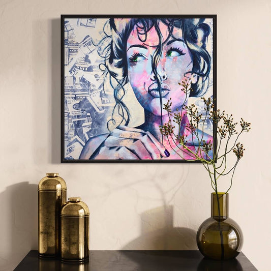 An abstract painting of a woman's face with vibrant blue and pink colors, displayed on a wall above a black console table with a vase of flowers.