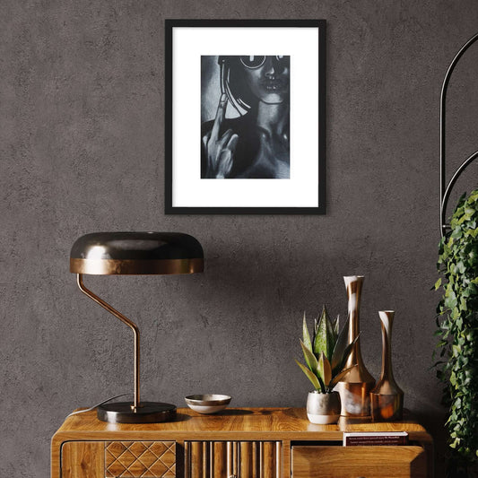 A framed black and white artwork depicting a woman making a hand gesture, displayed on a wall above a wooden console table with a plant and decorative items.