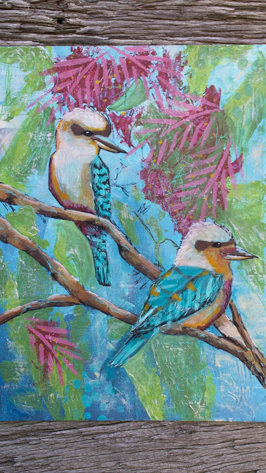 A vibrant painting of two Kookaburras perched on a branch with a vivid blue background and green leaves.